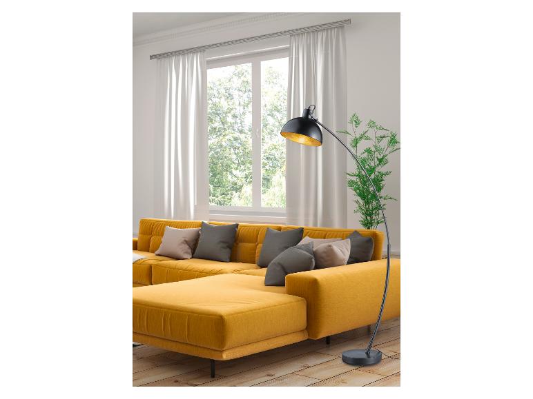 Gelbes Ecksofa mit Kissen, schwarze Stehlampe und großes Fenster mit weißen Vorhängen.