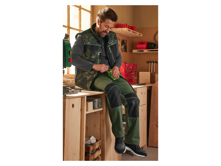 Ein Mann in einer Werkstatt trägt Parkside Arbeitskleidung und trinkt aus einer Flasche.