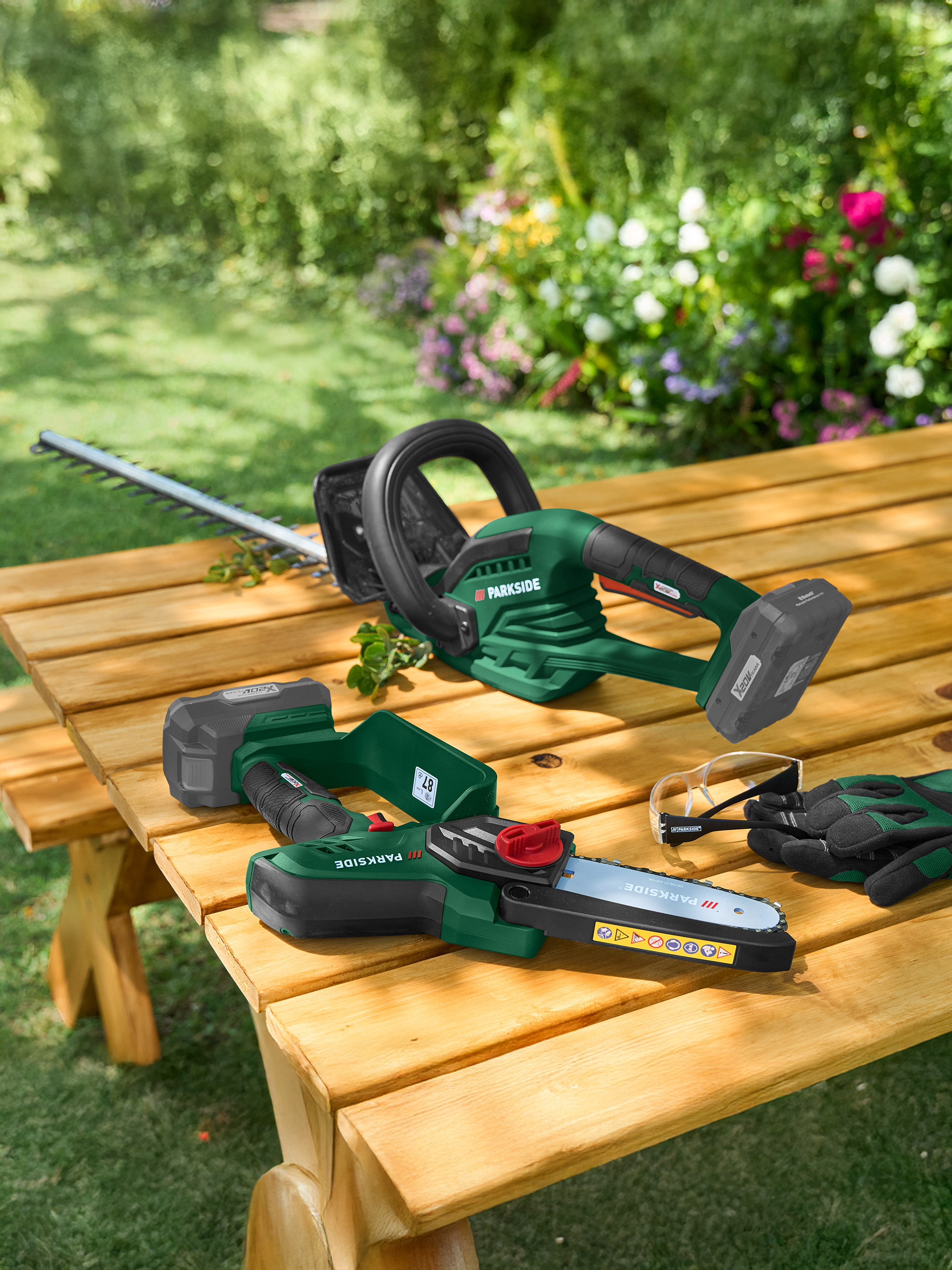 Heckenschere und Kettensäge auf einem Holztisch im Garten