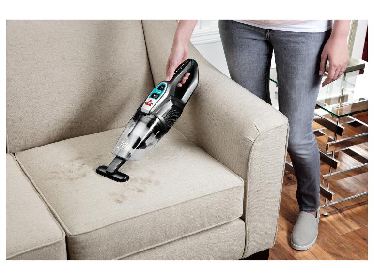 Frau reinigt ein Stoffsofa mit einem Bissell Handstaubsauger