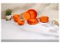 Oranges Geschirrset mit Tellern und Schüsseln, einer Topfpflanze und Besteck auf einer weißen Arbeitsplatte.