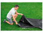 Ein Mann faltet eine schwarze Abdeckung für ein Trampolin auf dem Rasen.