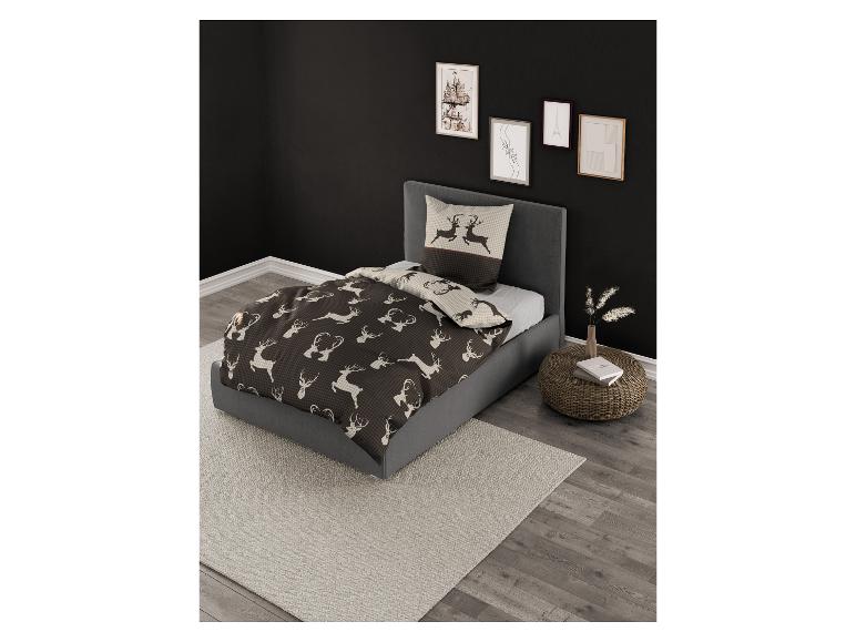 Bett mit grauem Rahmen und Rentier-Bettwäsche, daneben ein geflochtener Nachttisch.