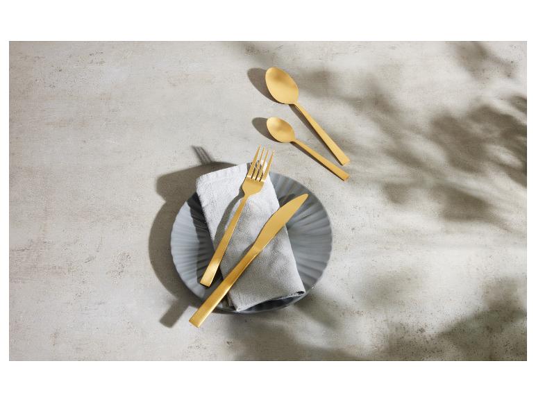 Goldenes Besteck auf einem grauen Teller mit Leinenserviette auf Betonhintergrund.