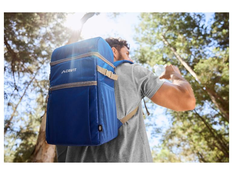 Mann mit blauem Kühlrucksack trinkt Wasser im Wald.