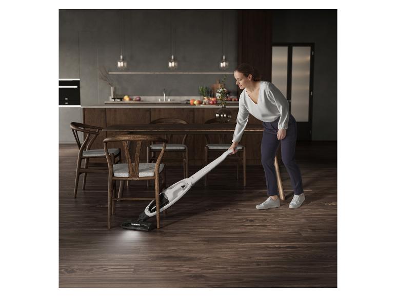 Frau saugt den Küchenboden mit einem kabellosen Staubsauger.