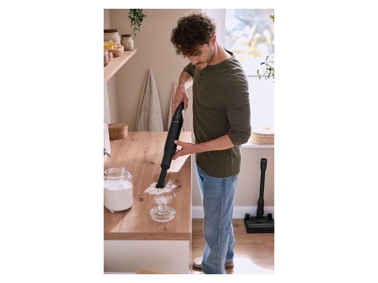 Mann reinigt Mehl von einer Holztheke mit einem Handstaubsauger