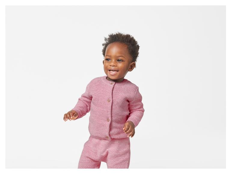 Ein kleines Kind lächelt in einem rosa Strickpullover und -hose.