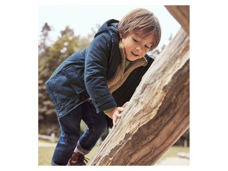 Ein Junge in dunkelblauer Jacke und Jeans klettert auf einen Baumstamm.