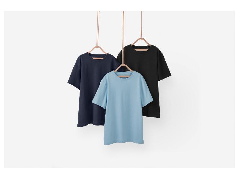Drei einfache T-Shirts in verschiedenen Farben hängen an Kleiderbügeln.