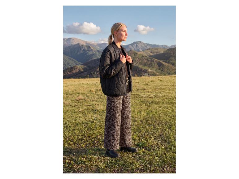 Frau in schwarzer Steppjacke und Leopardenmusterhose in einer Berglandschaft.
