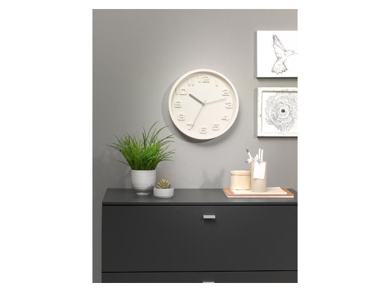 Weiße Wanduhr, Pflanzen und eine graue Kommode in minimalistischem Design.