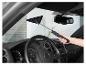 Person reinigt die Windschutzscheibe eines Autos von innen mit einem Reiniger mit Stiel.