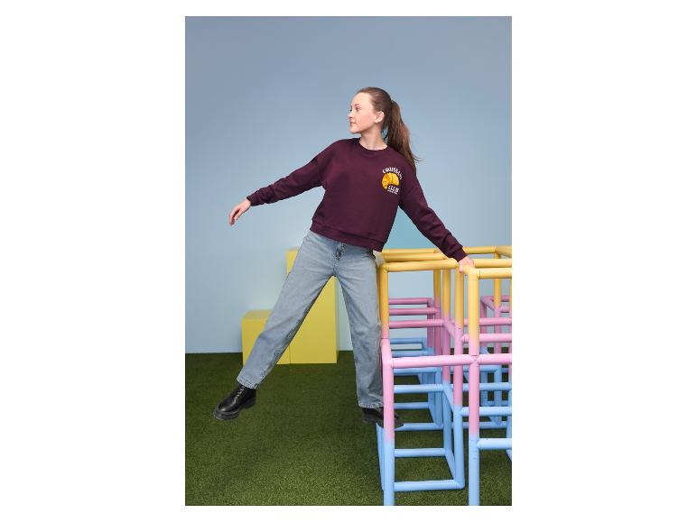 Mädchen in ESMARA KIDS Wide Leg Jeans und bordeauxrotem Sweatshirt auf einem bunten Klettergerüst
