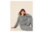 Frau in grauem Strickpullover und Hose, sitzend vor beigem Hintergrund.