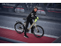 Frau in Radsportkleidung mit Helm und Handschuhen, lehnt an einem E-Bike auf einer Brücke.