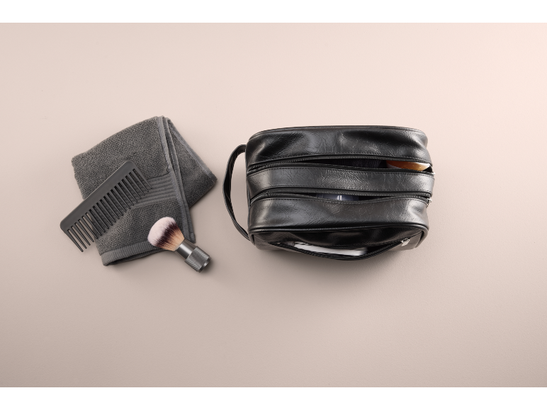 Schwarze Kulturtasche mit Kamm, Pinsel und grauem Handtuch.