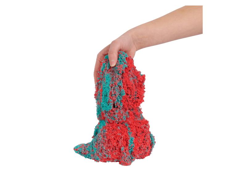 Eine Hand hält eine Portion roten und grünen kinetischen Sandes.