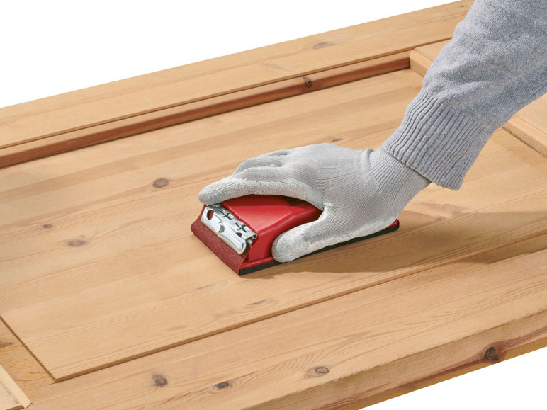 Eine Hand schleift eine Holztür mit einem Schleifblock.