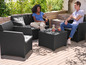Eine Frau und ein Mann sitzen auf einer schwarzen Wicker-Lounge-Garnitur mit passendem Couchtisch.