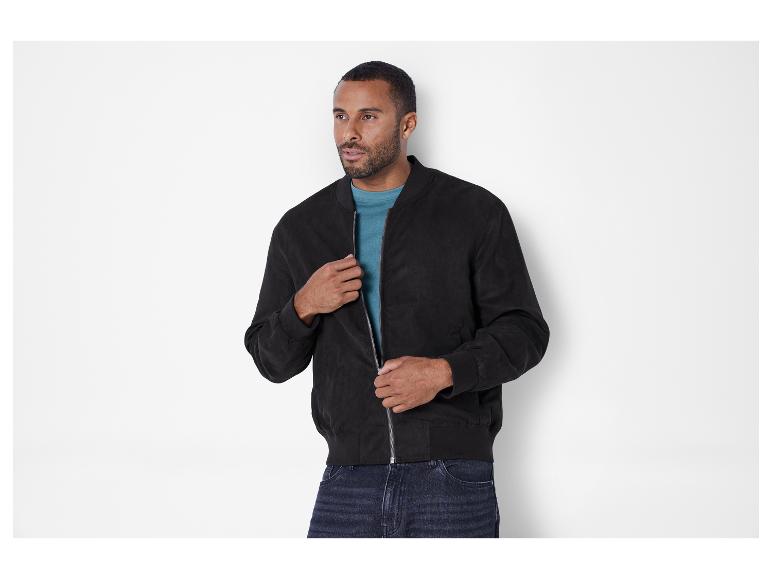 Ein Mann trägt eine schwarze Bomberjacke und Jeans.