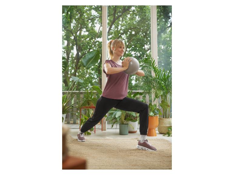 Frau in Sportkleidung macht Ausfallschritte mit einem kleinen grauen Gymnastikball.