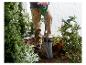 Person pflanzt mit einem Spaten in einem Garten mit Rosen und Büschen.