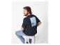 Mann in schwarzem T-Shirt mit Strandaufdruck und Jeans, auf einem Hocker sitzend.