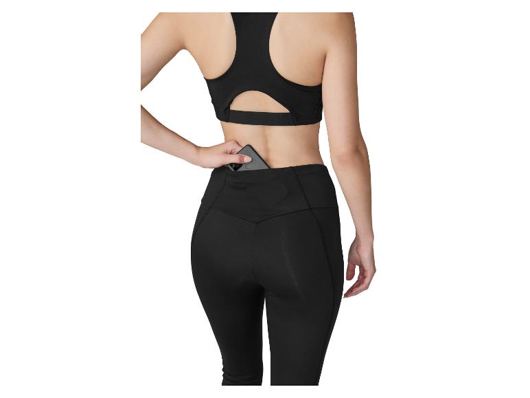 Frau in schwarzem Sport-BH und Leggings, die ein Telefon in die Gesäßtasche der Leggings steckt.