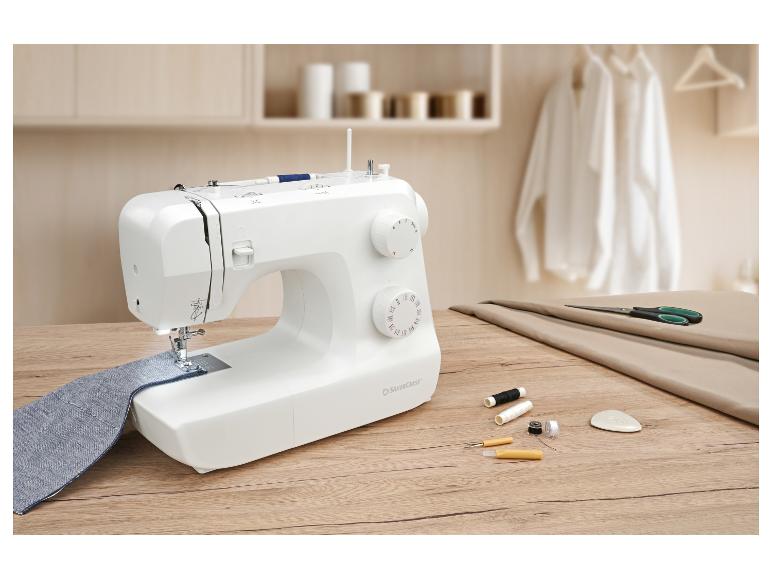 Nähmaschine mit blauem Stoff, Schere und Fäden auf einem Holztisch.
