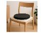 Heller Holzstuhl mit schwarzem rundem Sitzkissen in einem minimalistischen Interieur.