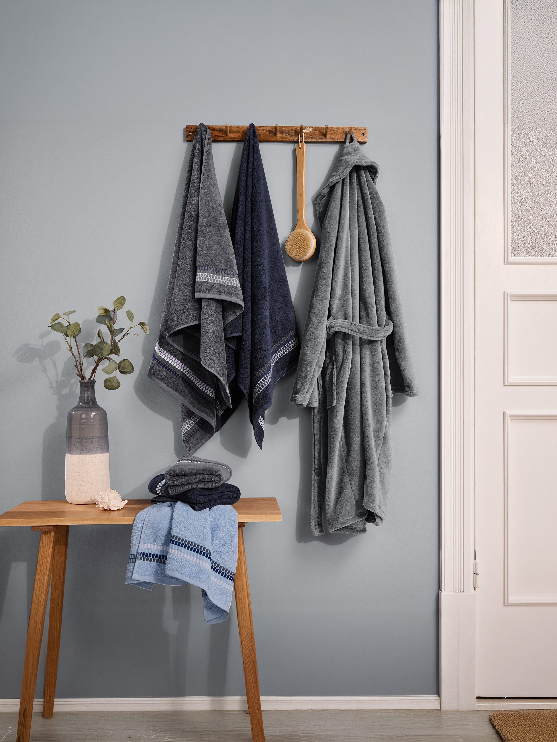 Handtücher und Bademantel in Blau- und Grautönen, an der Wand hängend.