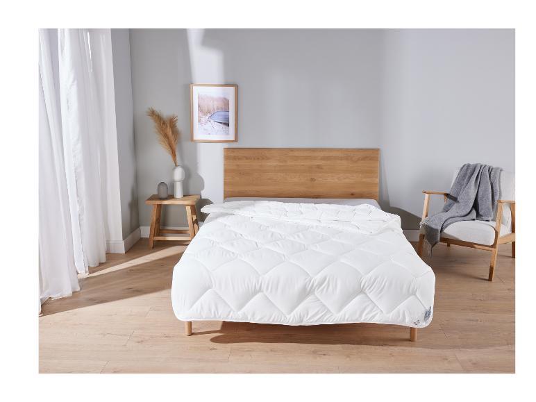 Eine weiße Bettdecke auf einem Holzbett mit einem Stuhl daneben.