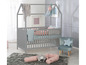 Ein graues Babybett mit Haus-förmigem Rahmen, ein graues Samt-Stuhl und rosa Kissen.