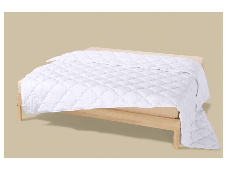 Weiße Steppdecke auf einem Holzbett mit beigem Laken.