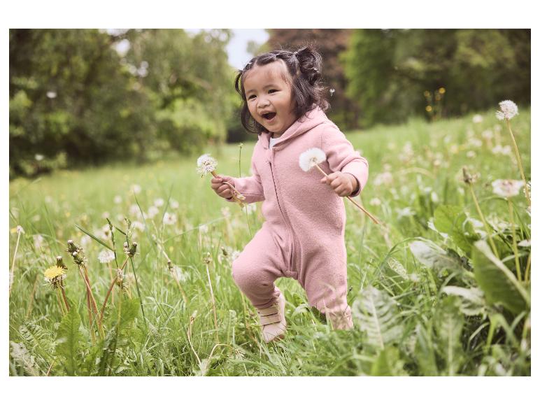 Kleinkind im rosa LUPILU® Baby Wollwalk-Overall beim Spielen auf einer Wiese