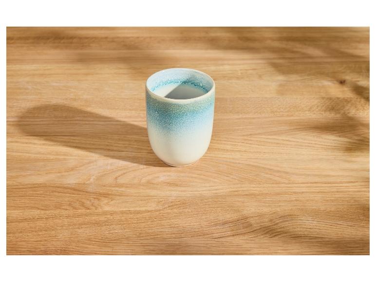 Eine blau-weiße Keramiktasse auf einem hellen Holztisch mit Schatten.