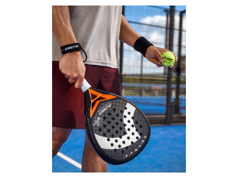 Padel-Schläger und Ball, gehalten von einem Spieler auf einem Padel-Platz.