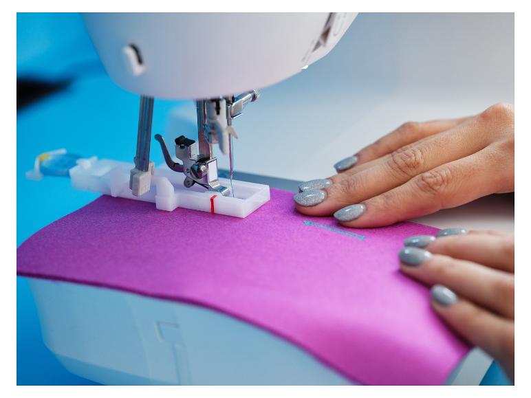 Frau näht lila Stoff mit Nähmaschine.