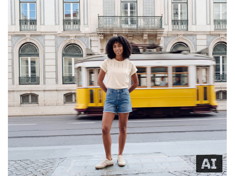 Frau in beigem Pointelle-T-Shirt und Denim-Shorts vor einer gelben Straßenbahn.