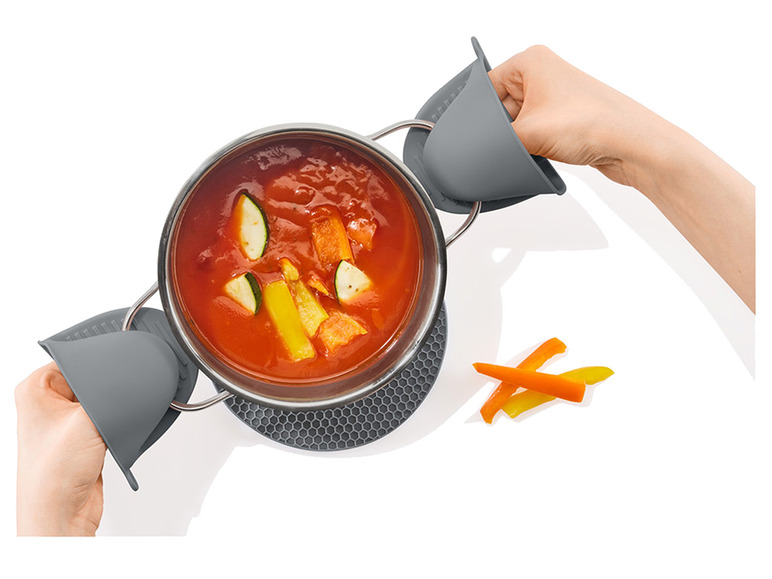 Ein Topf mit Suppe, grauen Silikon-Topflappen und einer hitzebeständigen Unterlage.