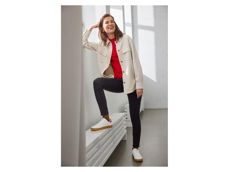 Frau in beigem Hemd, rotem T-Shirt und schwarzen Jeans mit Leoparden-Socken und weißen Sneakern.