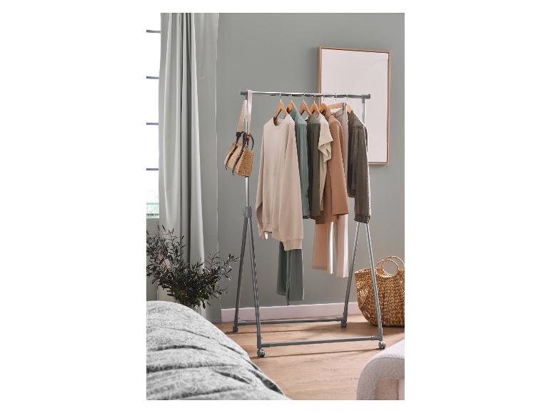 Kleiderständer mit Kleidung in verschiedenen Farben, einer Tasche und einem Korb in einem Raum.