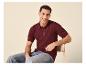 Mann in einem burgunderroten Strick-Poloshirt und Jeans, auf einem Stuhl sitzend.