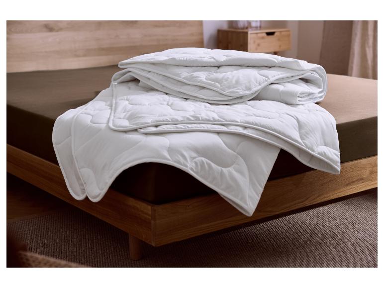 Weiße gesteppte Bettdecke auf einem braunen Bett mit Holzrahmen.