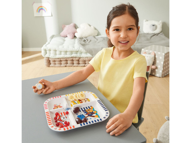 Ein Kind isst von einem Paw Patrol-Teller mit Banane, Trauben und Beeren.
