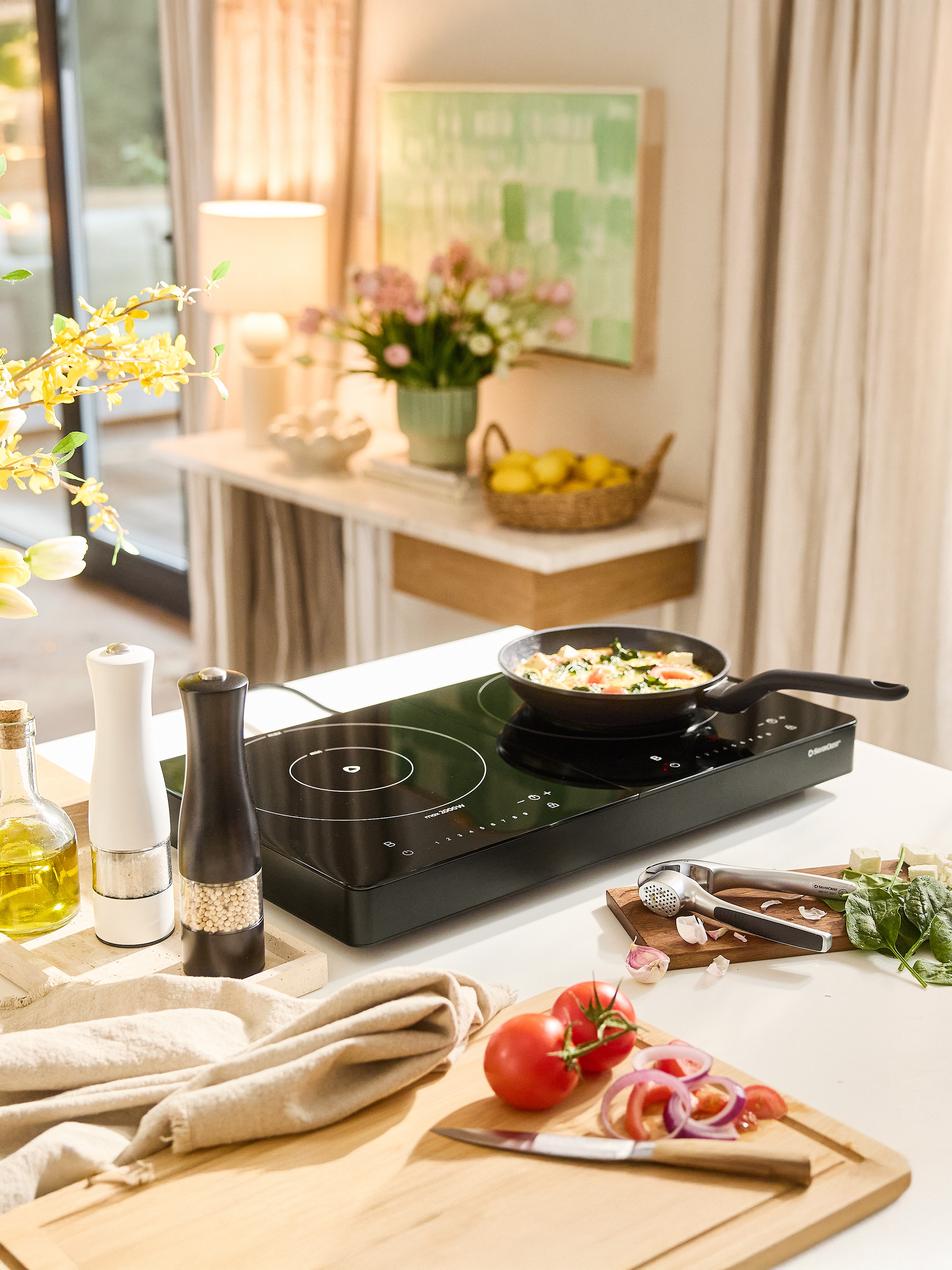 SilverCrest Induktionskochfeld mit Pfanne, Gewürzen und frischem Gemüse auf einer Küchenarbeitsplatte.