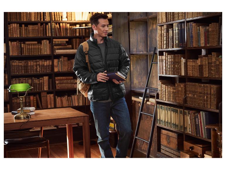 Mann in schwarzer Steppjacke und Jeans, hält Bücher in einer Bibliothek.