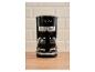 Schwarze Kaffeemaschine mit Kanne, mit der Aufschrift „1973“ vor beigen Fliesen.