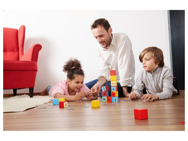 Vater und Kinder spielen auf dem Boden mit Lernbausteinen und Karten.